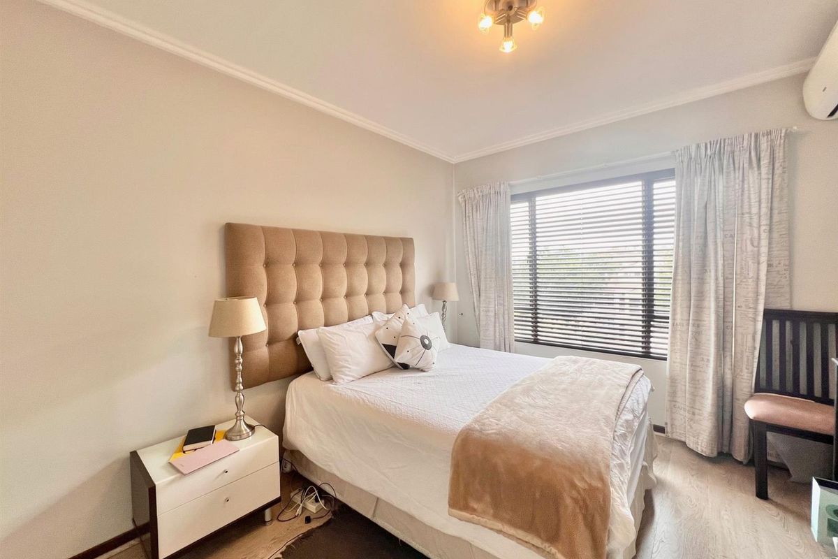 A well-maintained bedroom featuring laminate flooring, venetian blinds, and a wall-mounted air conditioning unit.