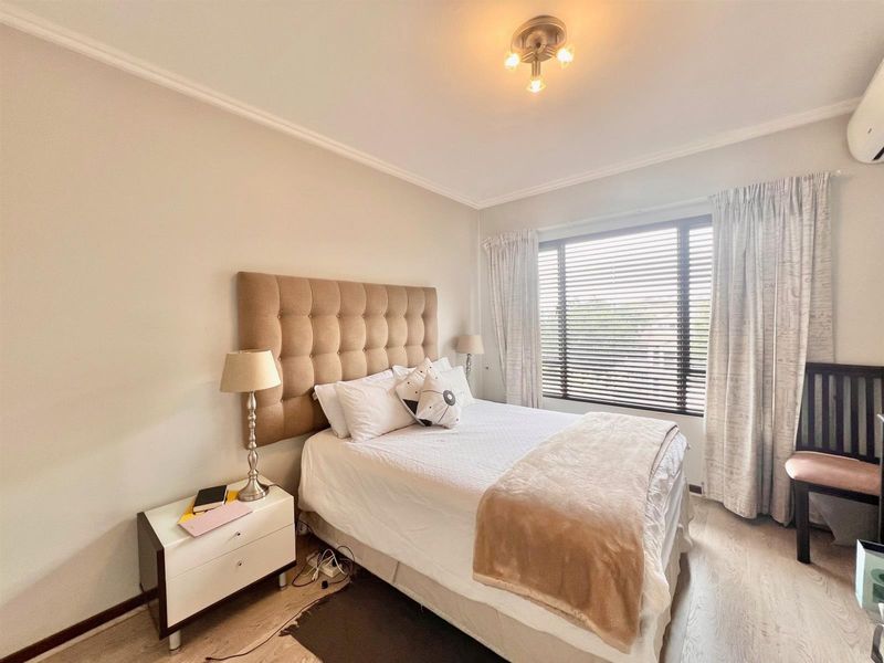 A well-maintained bedroom featuring laminate flooring, venetian blinds, and a wall-mounted air conditioning unit.