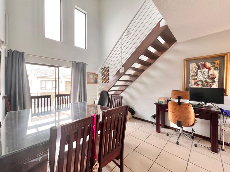 Open plan living area featuring double volume ceilings, tiled flooring, and a wooden staircase leading to the upper level.