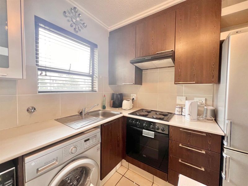 Compact kitchen featuring dark wood cabinetry, integrated oven and hob, stainless steel sink, and tiled backsplash with neutral finishes.
