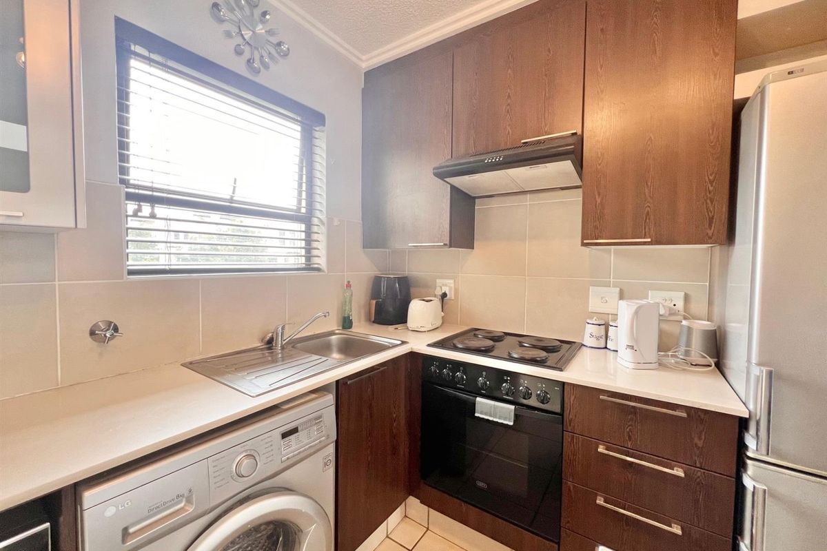Compact kitchen featuring dark wood cabinetry, integrated oven and hob, stainless steel sink, and tiled backsplash with neutral finishes.