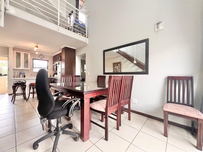 Open plan living and dining area featuring tiled floors, a mezzanine level with metal railing, and an integrated kitchen with breakfast bar.