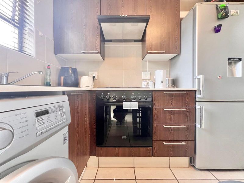 Compact kitchen featuring dark wood-finish cabinetry, built-in oven with hob, extractor fan, tiled backsplash, and tiled flooring.