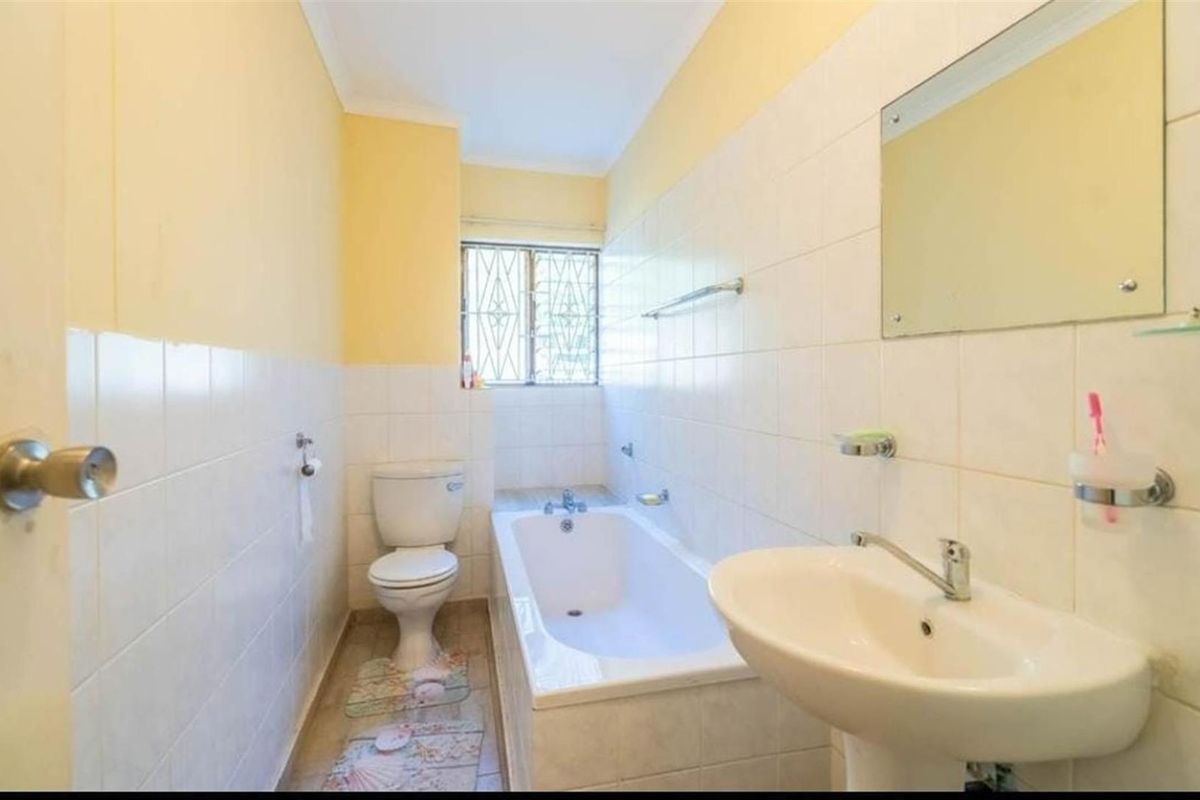 A functional bathroom featuring a bathtub, pedestal basin, and toilet with tiled walls and security bars on the window.