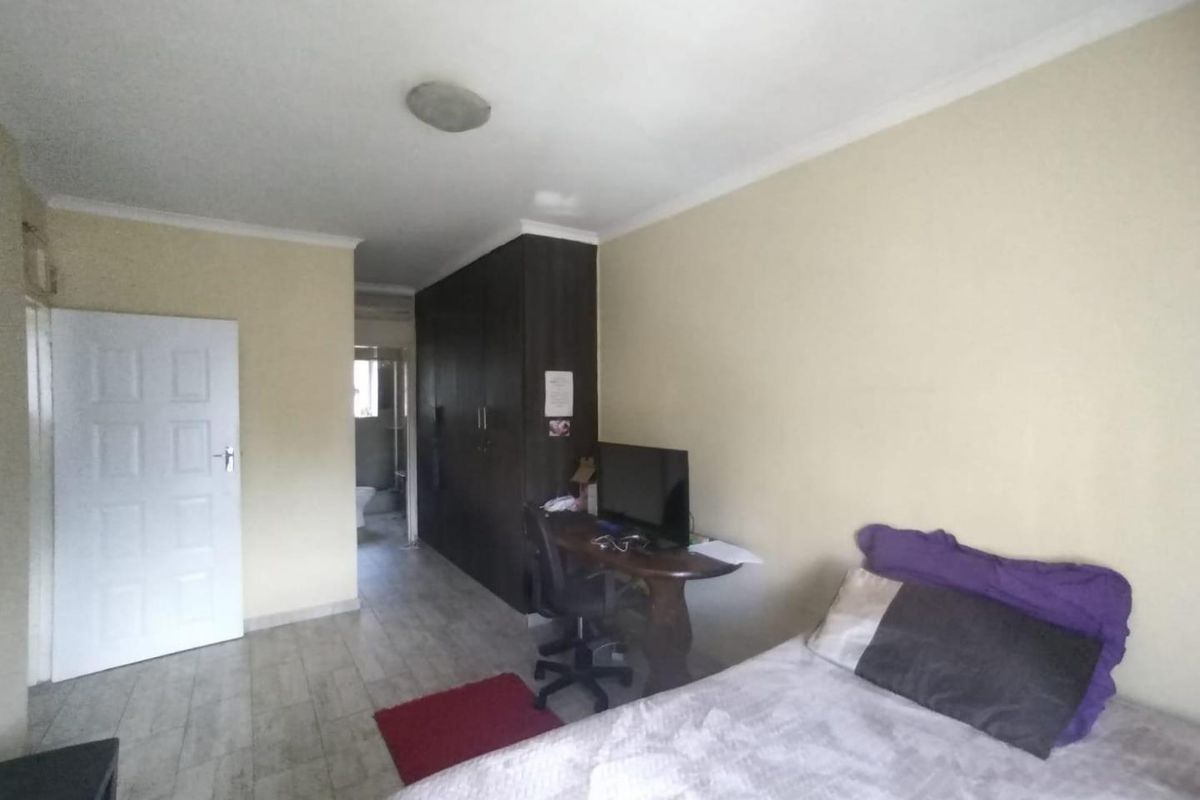 A bedroom featuring built-in cupboards, tiled flooring, and a neutral wall finish, with an adjacent view into a bathroom area.