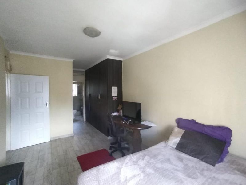 A bedroom featuring built-in cupboards, tiled flooring, and a neutral wall finish, with an adjacent view into a bathroom area.