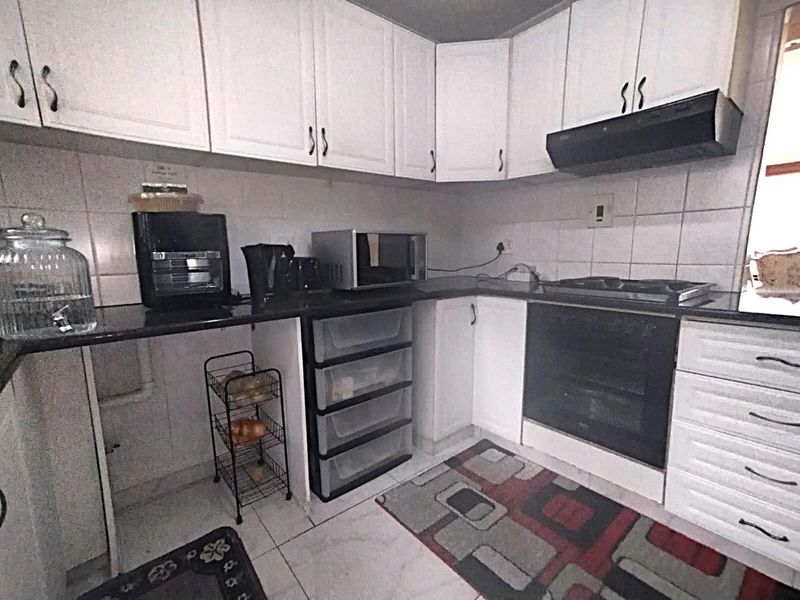 A functional kitchen featuring white cabinetry, black granite countertops, a built-in oven, and a gas hob with an extractor fan.