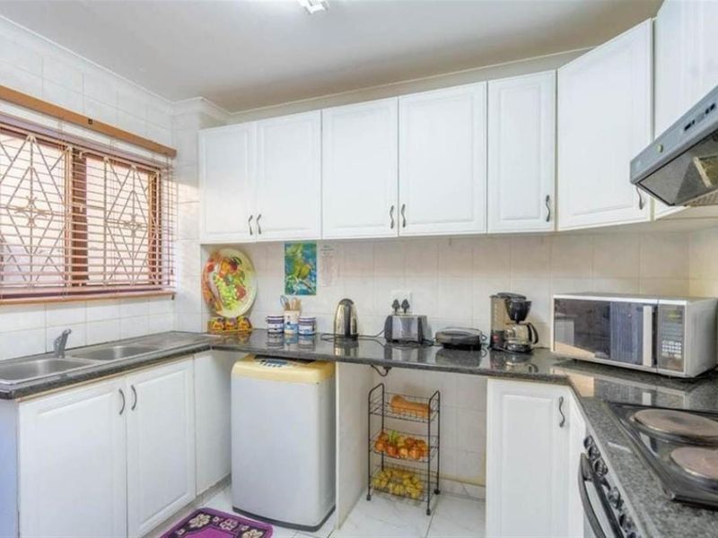 A functional kitchen featuring white cabinetry, granite countertops, a tiled backsplash, and built-in cooking appliances, offering a clean and practical workspace.