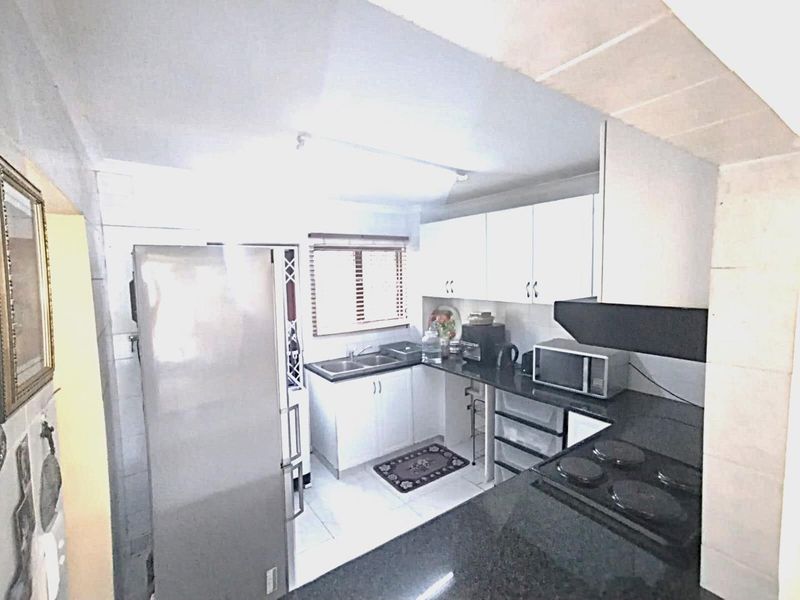 Compact kitchen featuring white cabinetry, dark granite countertops, an electric hob, and a double sink with tiled flooring.