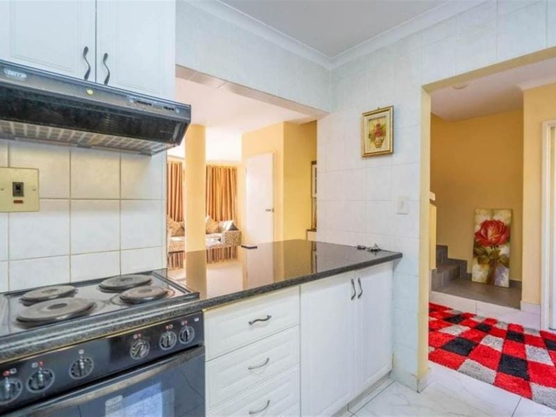A functional kitchen featuring white cabinetry, granite countertops, a built-in electric stove with an extractor fan, and tiled splashbacks.