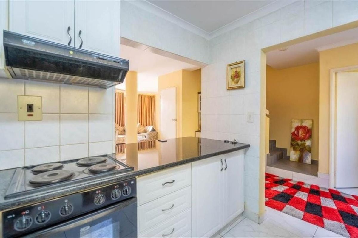 A functional kitchen featuring white cabinetry, granite countertops, a built-in electric stove with an extractor fan, and tiled splashbacks.
