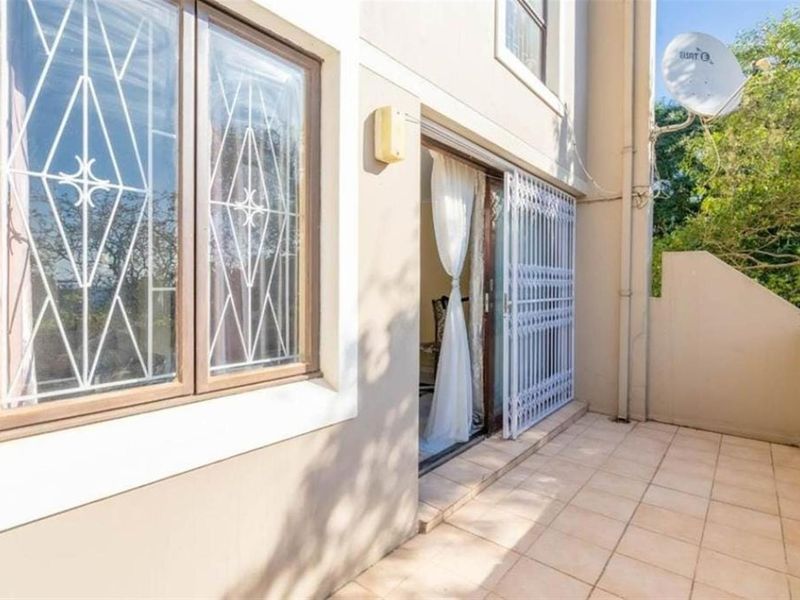 A tiled balcony area featuring a security gate and window security bars, providing an outdoor space accessible from the interior.