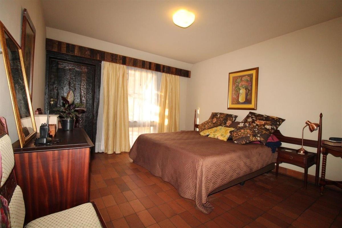 A bedroom featuring terracotta floor tiles and a dark wood door with a rustic timber header.