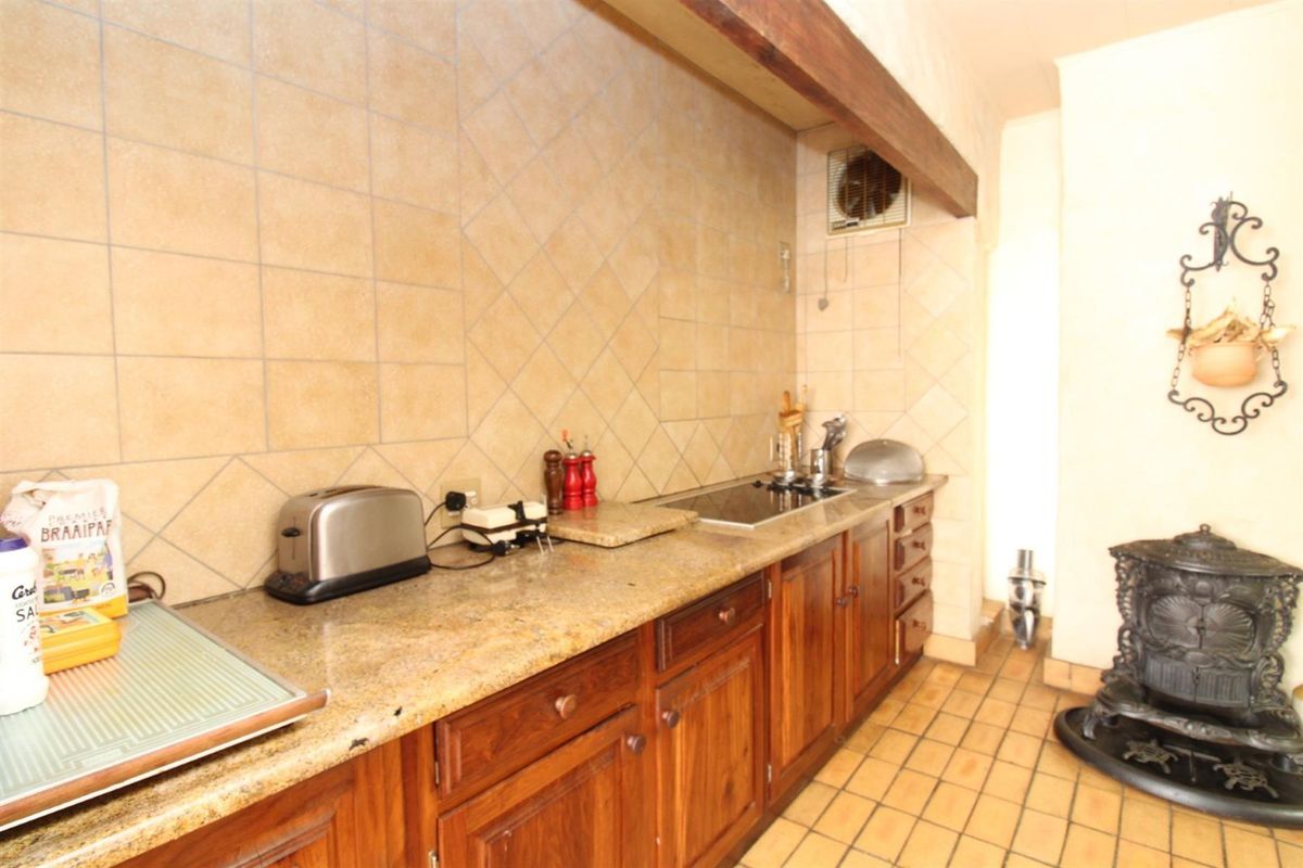 A functional kitchen area featuring wooden cabinetry, stone countertops, a built-in hob, and a traditional cast-iron fireplace.