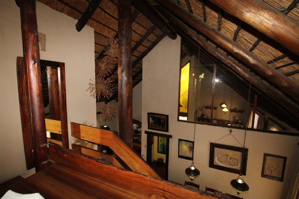A view from a mezzanine level overlooking a living area, featuring a high vaulted thatched roof with exposed timber beams and wooden support pillars.