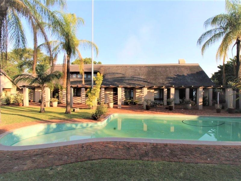 Rear view of a traditional thatched-roof house featuring a covered patio, landscaped garden, and a swimming pool.