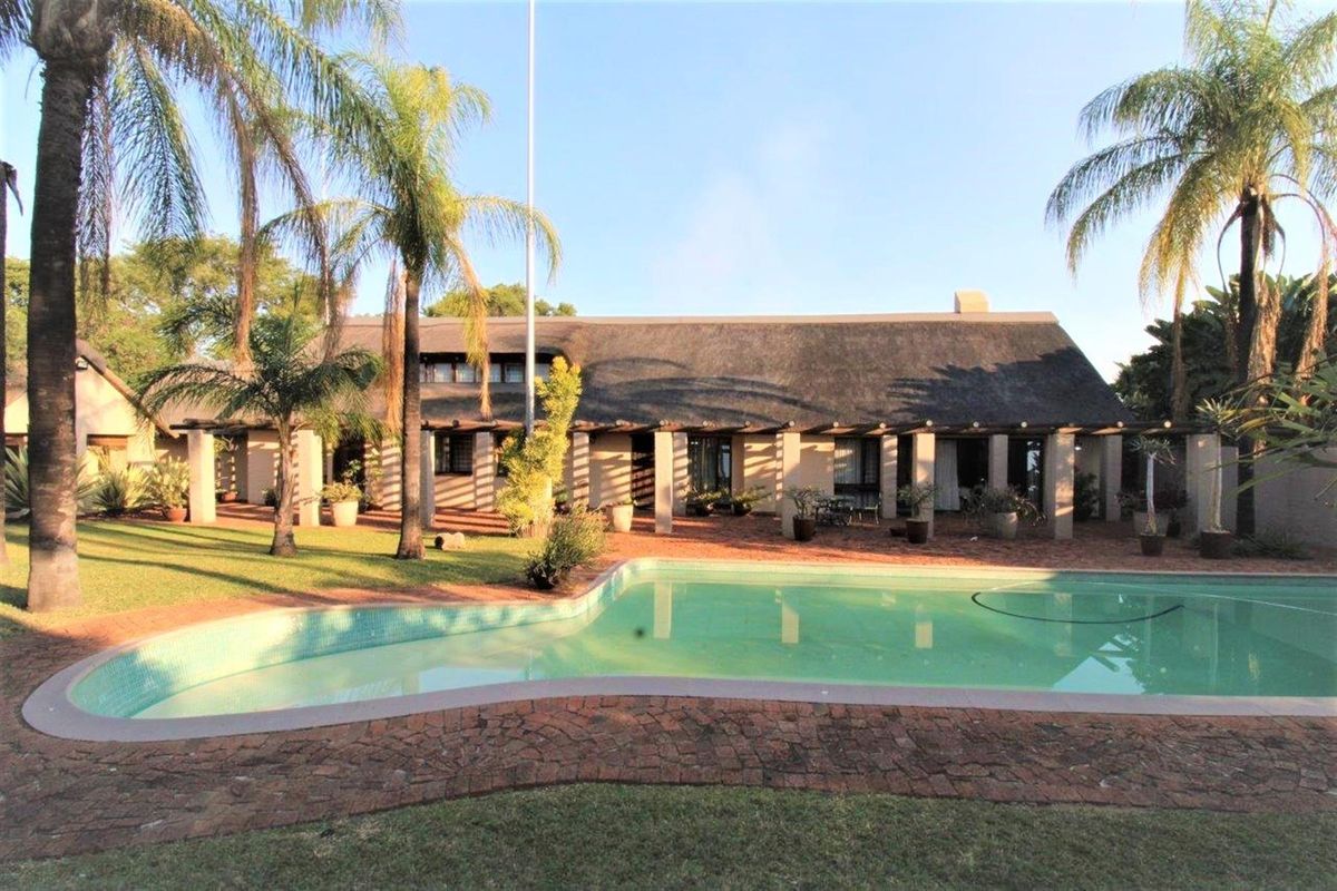 Rear view of a traditional thatched-roof house featuring a covered patio, landscaped garden, and a swimming pool.