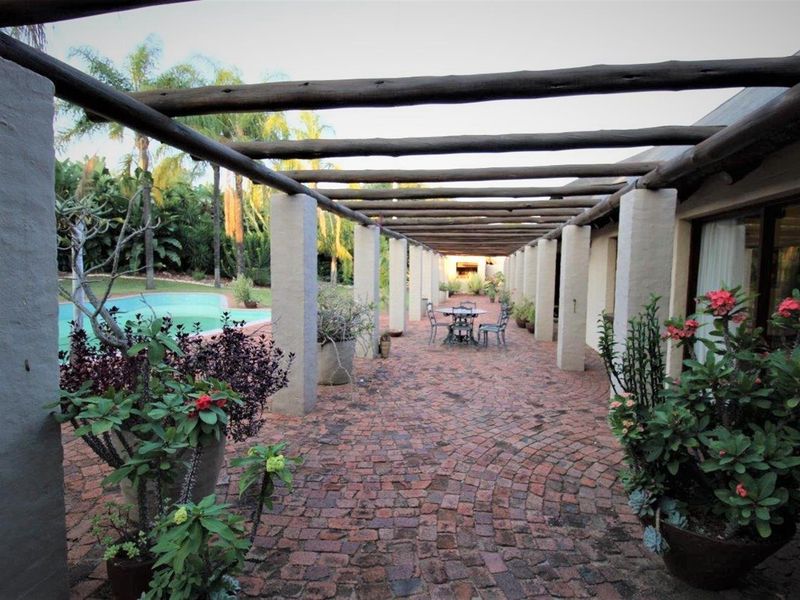 A spacious covered patio featuring a rustic timber pergola, brick paving, and direct access to the garden and swimming pool area.