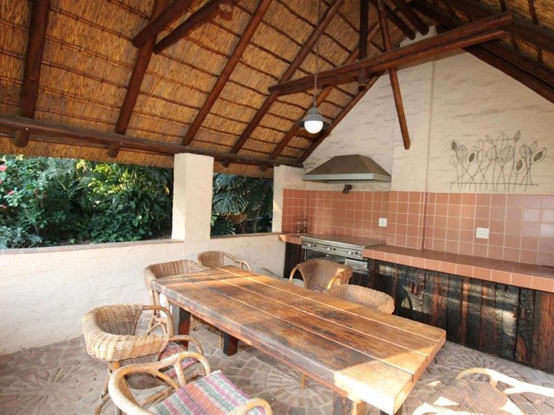 Covered outdoor patio featuring a built-in braai area with tiled countertops, rustic cabinetry, and a traditional thatched roof structure.