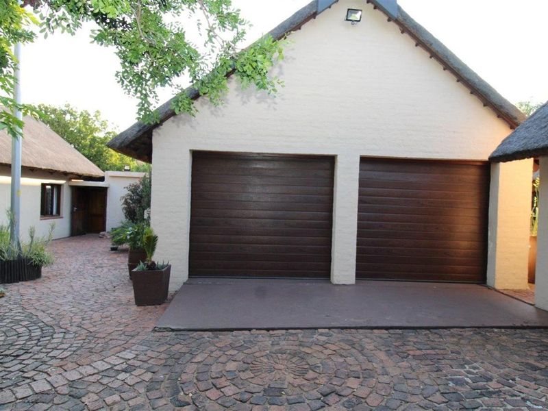 A double garage with dark brown sectional doors, featuring a traditional thatched roof and a paved driveway area.