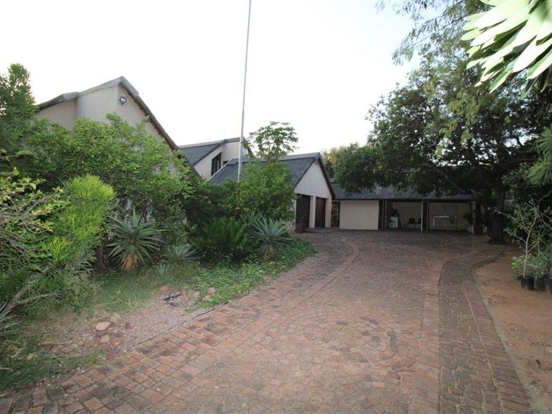 Front exterior view of the property featuring a paved driveway leading to a multi-car garage and established garden surroundings.