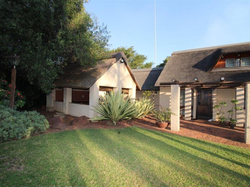 A charming thatched-roof residence featuring a paved patio area, well-maintained garden, and established landscaping, offering a classic and inviting exterior aesthetic.