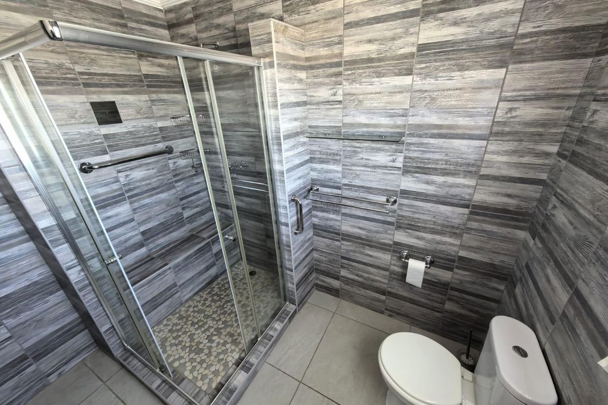 Modern bathroom featuring a glass-enclosed shower with pebble-style floor tiling, wall-mounted toilet, and contemporary wood-look wall tiles.
