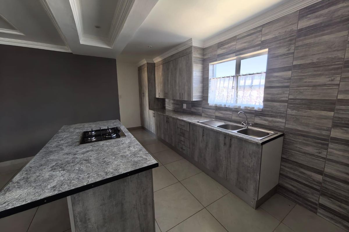 Modern kitchen featuring wood-look cabinetry, stone-patterned countertops, a central island with a built-in gas hob, and a double stainless steel sink.