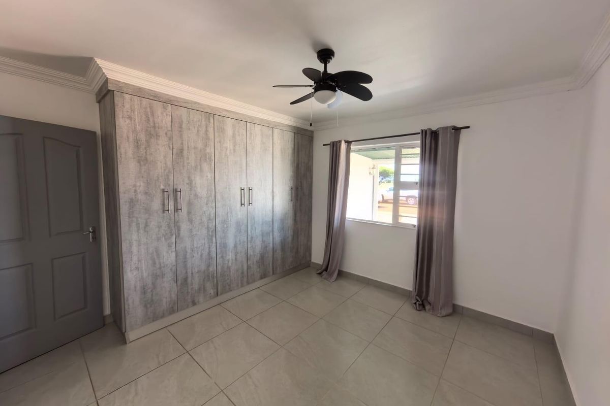 A clean, well-maintained bedroom featuring large built-in cupboards with a modern wood-grain finish, tiled flooring, and a ceiling fan.
