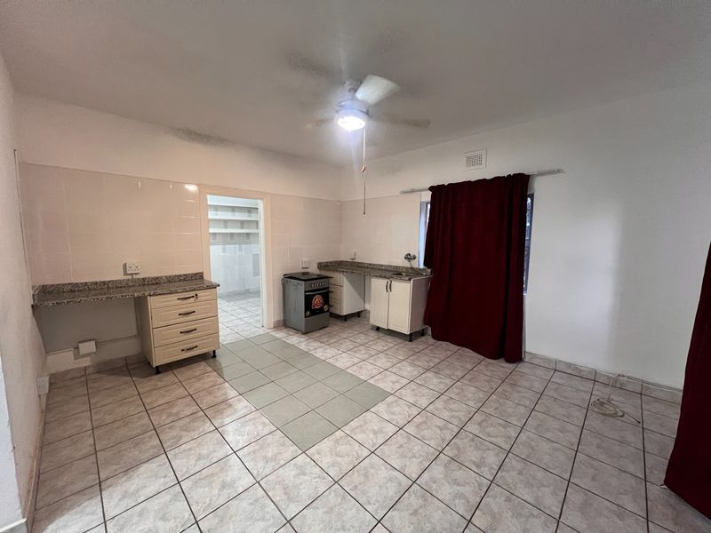 A functional kitchen area featuring tiled flooring, granite-look countertops, built-in cabinetry, and a freestanding stove, with an adjacent walk-in pantry or scullery space.