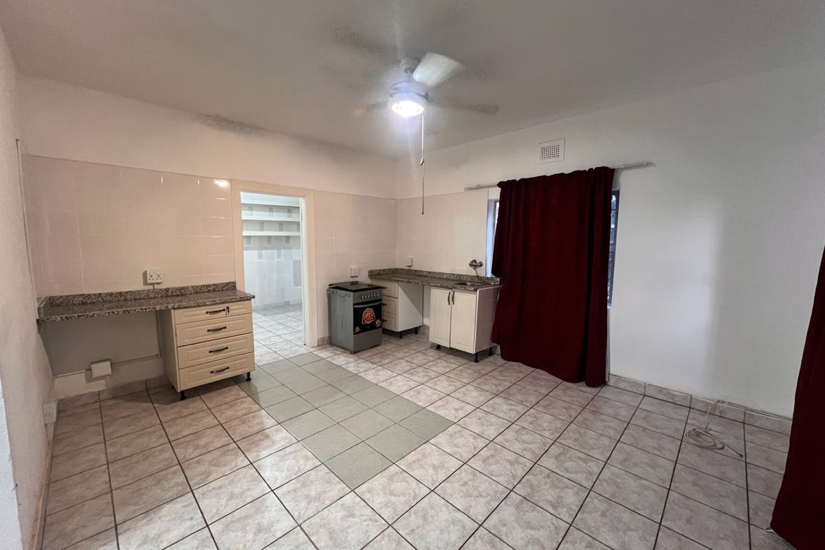 A functional kitchen area featuring tiled flooring, granite-look countertops, built-in cabinetry, and a freestanding stove, with an adjacent walk-in pantry or scullery space.