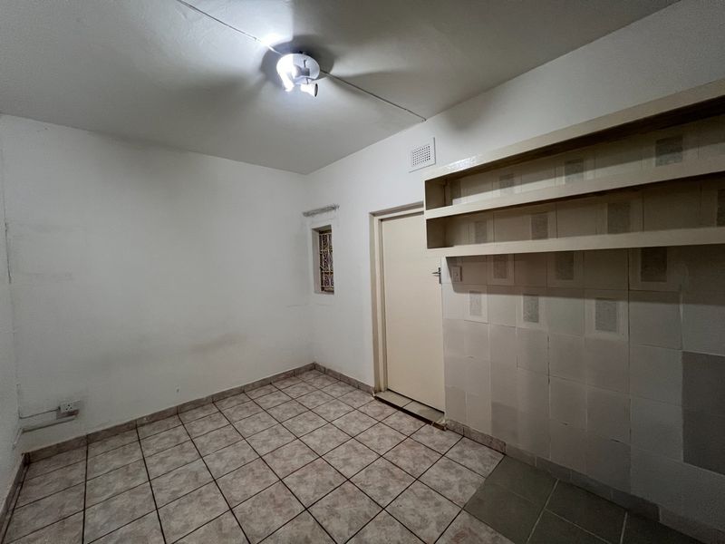 A functional utility space or scullery featuring tiled flooring, built-in wall shelving, and a small window with security bars.