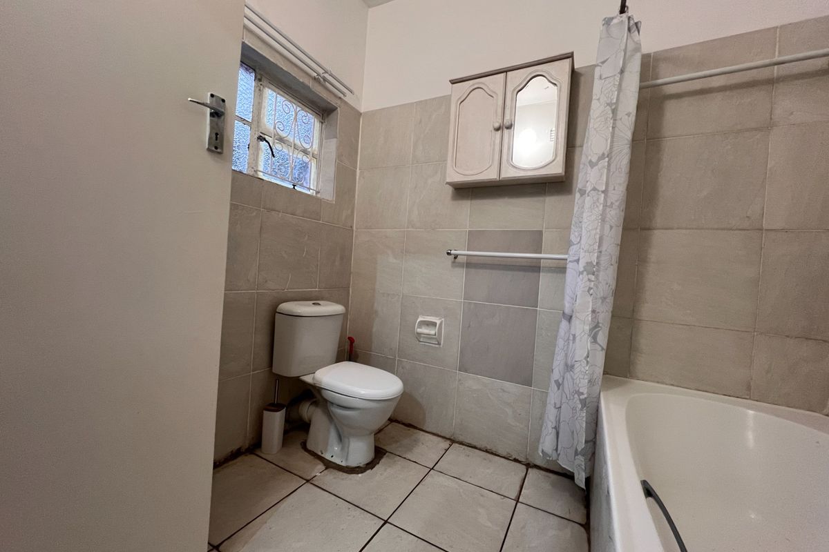 A functional bathroom featuring a standard bathtub, toilet, wall-mounted medicine cabinet, and tiled walls and flooring.