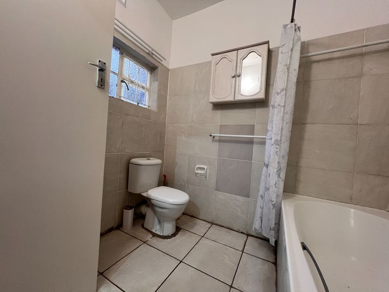 A functional bathroom featuring a standard bathtub, toilet, wall-mounted medicine cabinet, and tiled walls and flooring.