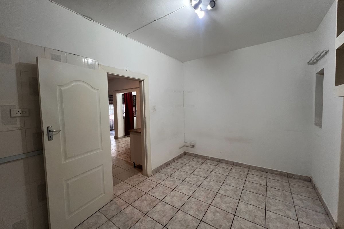 An empty, tiled room featuring a central ceiling light and a doorway leading to an adjacent living area.