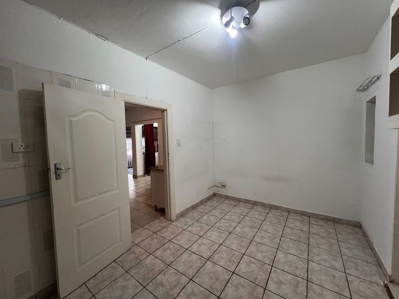 An empty, tiled room featuring a central ceiling light and a doorway leading to an adjacent living area.