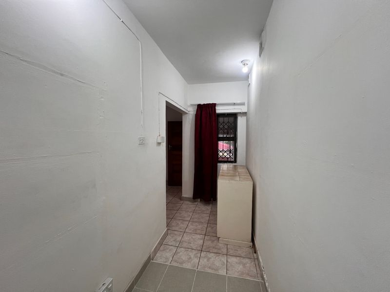 A narrow hallway featuring tiled flooring, a small window with security bars, and exposed electrical conduit along the wall.