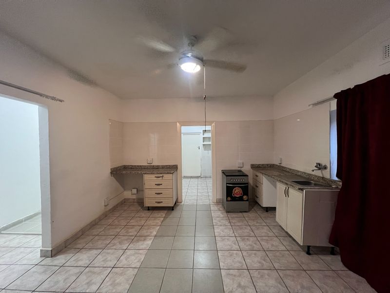 A functional kitchen featuring tiled flooring, granite-look countertops, built-in cabinetry, and a freestanding stove, with a central ceiling fan and direct access to adjacent rooms.
