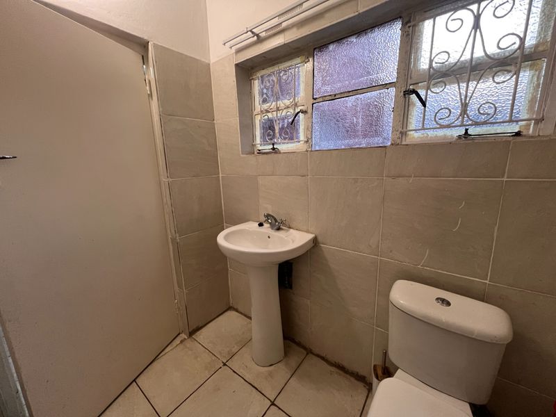 A compact bathroom featuring a pedestal basin, toilet, and tiled walls with obscured glass windows and security bars.