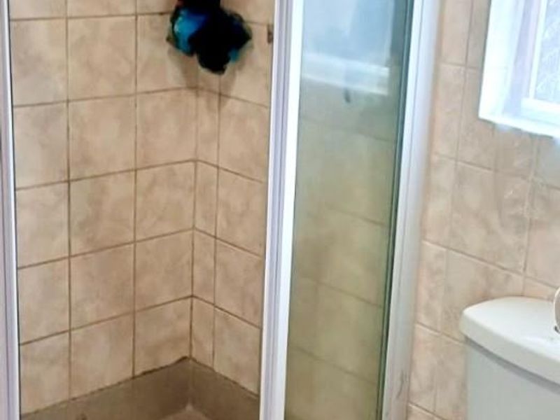 A functional bathroom featuring a corner shower enclosure with a glass door, tiled walls, and a standard white toilet.