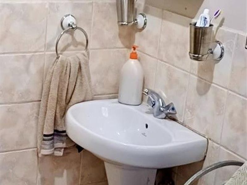 A compact bathroom featuring a white pedestal basin, wall-mounted medicine cabinet, and neutral ceramic wall tiling.