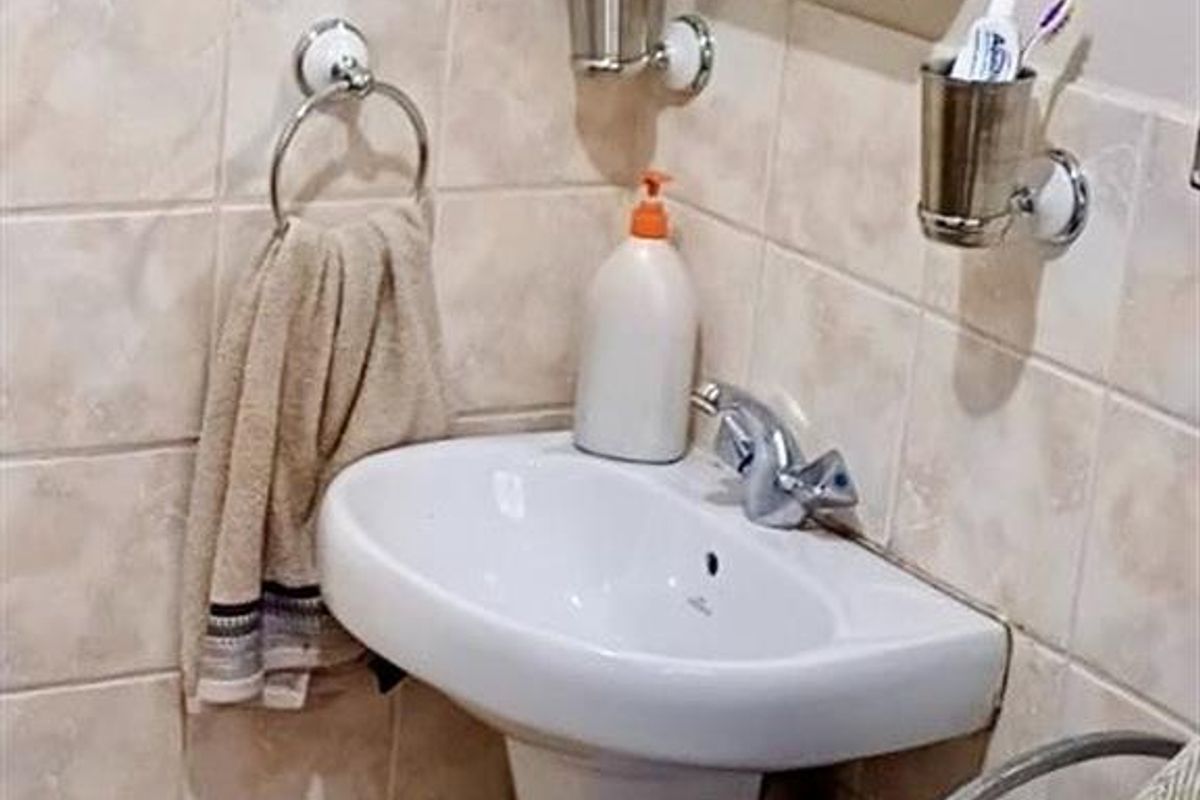 A compact bathroom featuring a white pedestal basin, wall-mounted medicine cabinet, and neutral ceramic wall tiling.