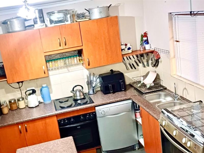 A functional kitchen featuring wood-tone cabinetry, laminate countertops, a built-in oven with hob, and a double-basin sink with tiled splashbacks.
