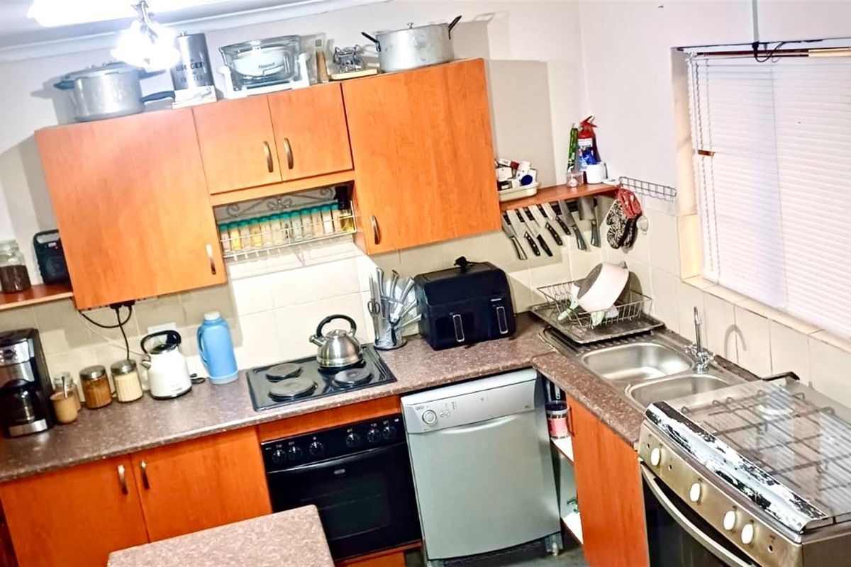 A functional kitchen featuring wood-tone cabinetry, laminate countertops, a built-in oven with hob, and a double-basin sink with tiled splashbacks.