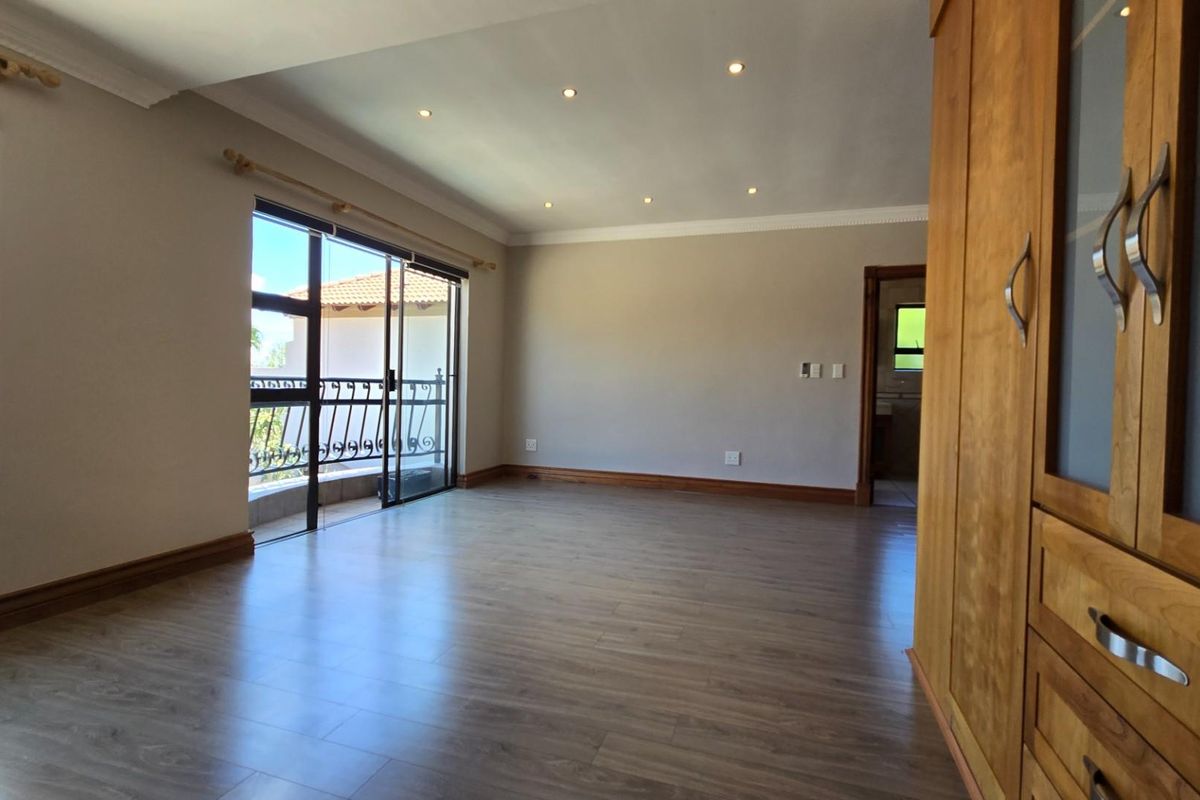 Spacious bedroom featuring wood-look laminate flooring, recessed ceiling lighting, and sliding glass doors opening onto a private balcony.