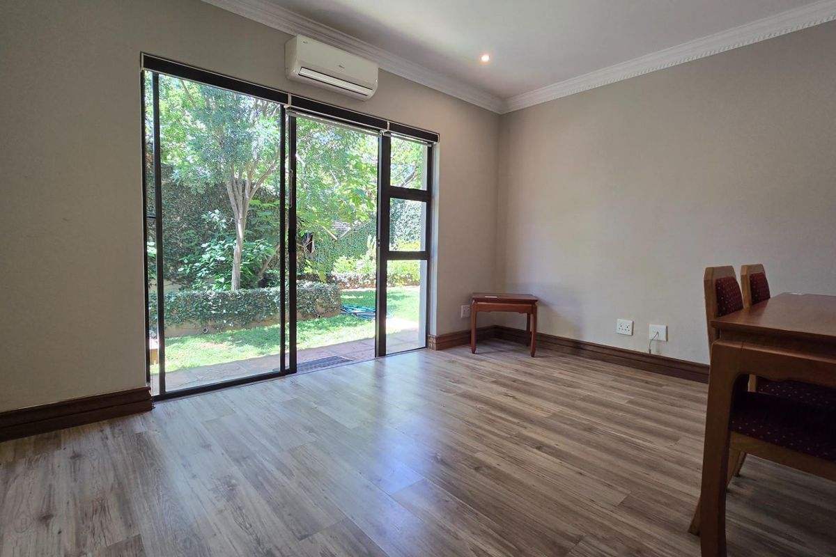 A bright living area featuring wood-look laminate flooring, crown molding, and large sliding glass doors providing direct access to the garden.