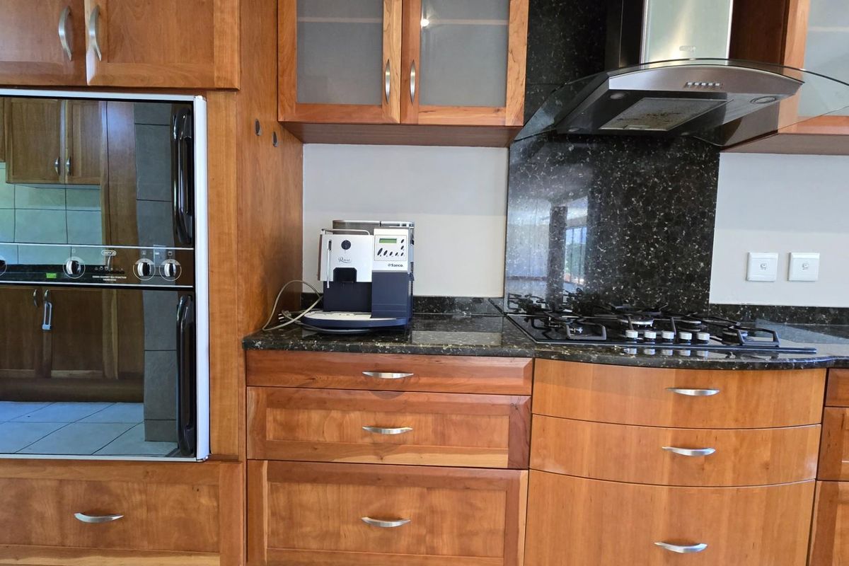 A kitchen featuring warm-toned wooden cabinetry, dark granite countertops, a built-in oven, and a stainless steel extractor fan.