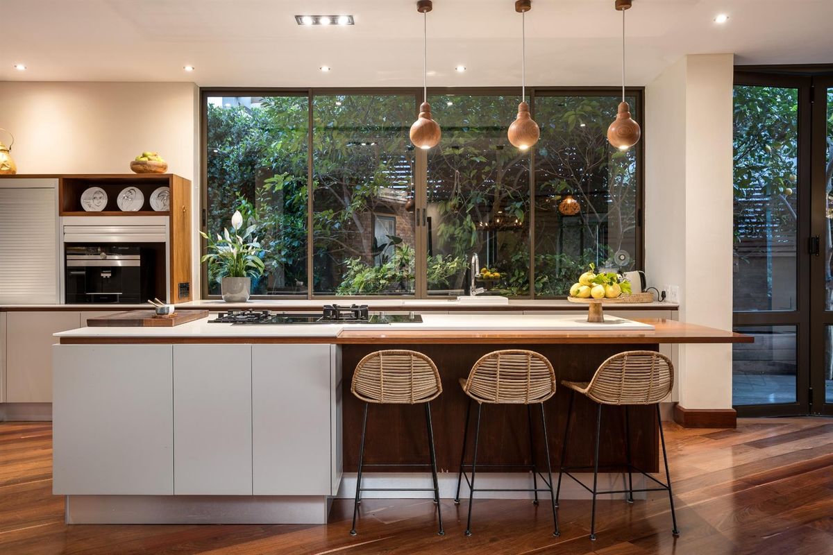 Modern kitchen featuring a central island with a built-in gas hob, wooden breakfast bar, and large windows overlooking a lush garden.