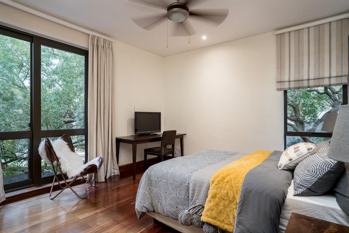 A well-lit bedroom featuring polished hardwood flooring, large windows with garden views, and a ceiling fan.
