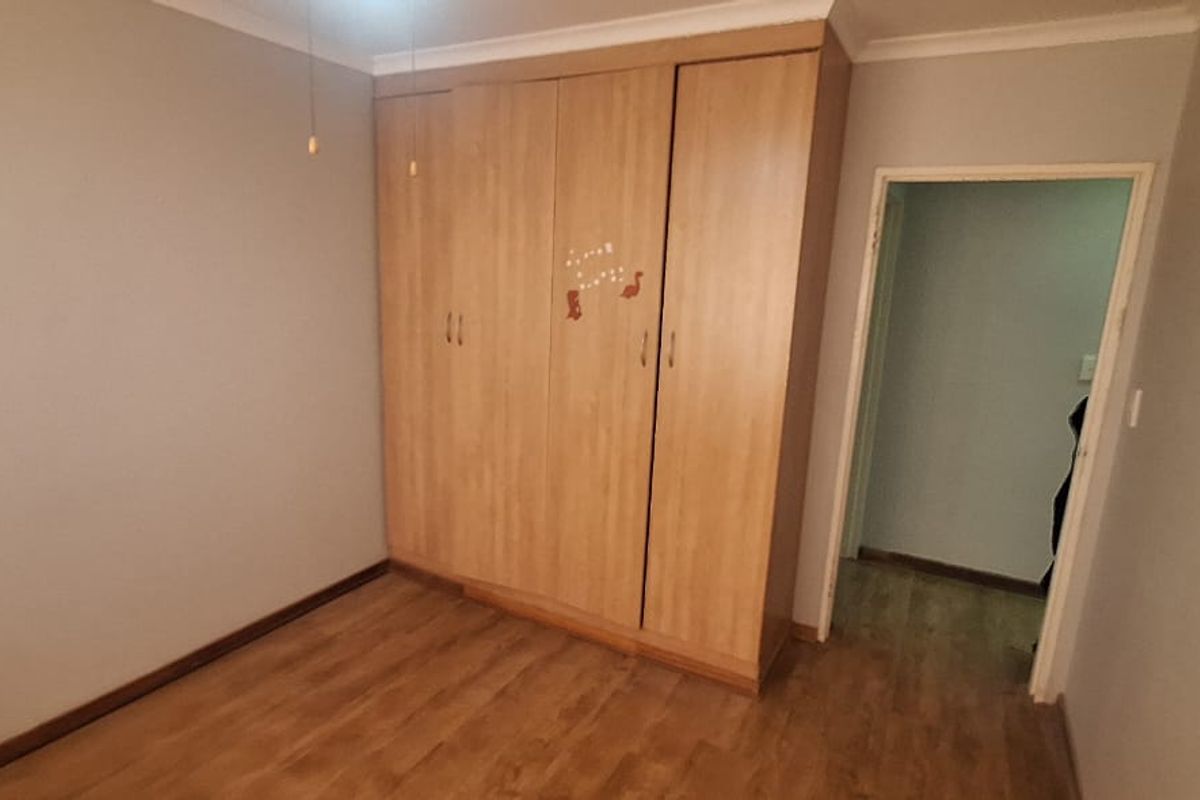A bedroom featuring built-in wooden wardrobes, laminate flooring, and neutral wall tones, providing a functional and clean living space.